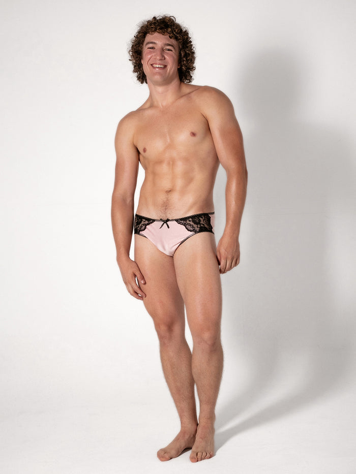 Man wearing pink underwear with black lace details on a white background