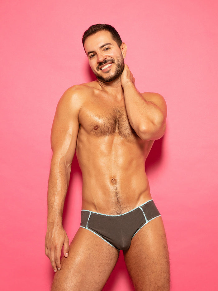 Man wearing grey panties with blue lace trim against a pink background.