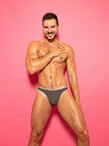Front view of a man wearing a grey thong panty with blue lace trim, against a pink background.