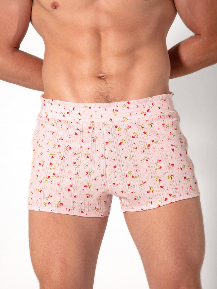 Man wearing pink shorts with a red floral pattern on a plain background