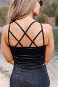Person wearing a black tank top with criss-cross straps and patterned pants outdoors.